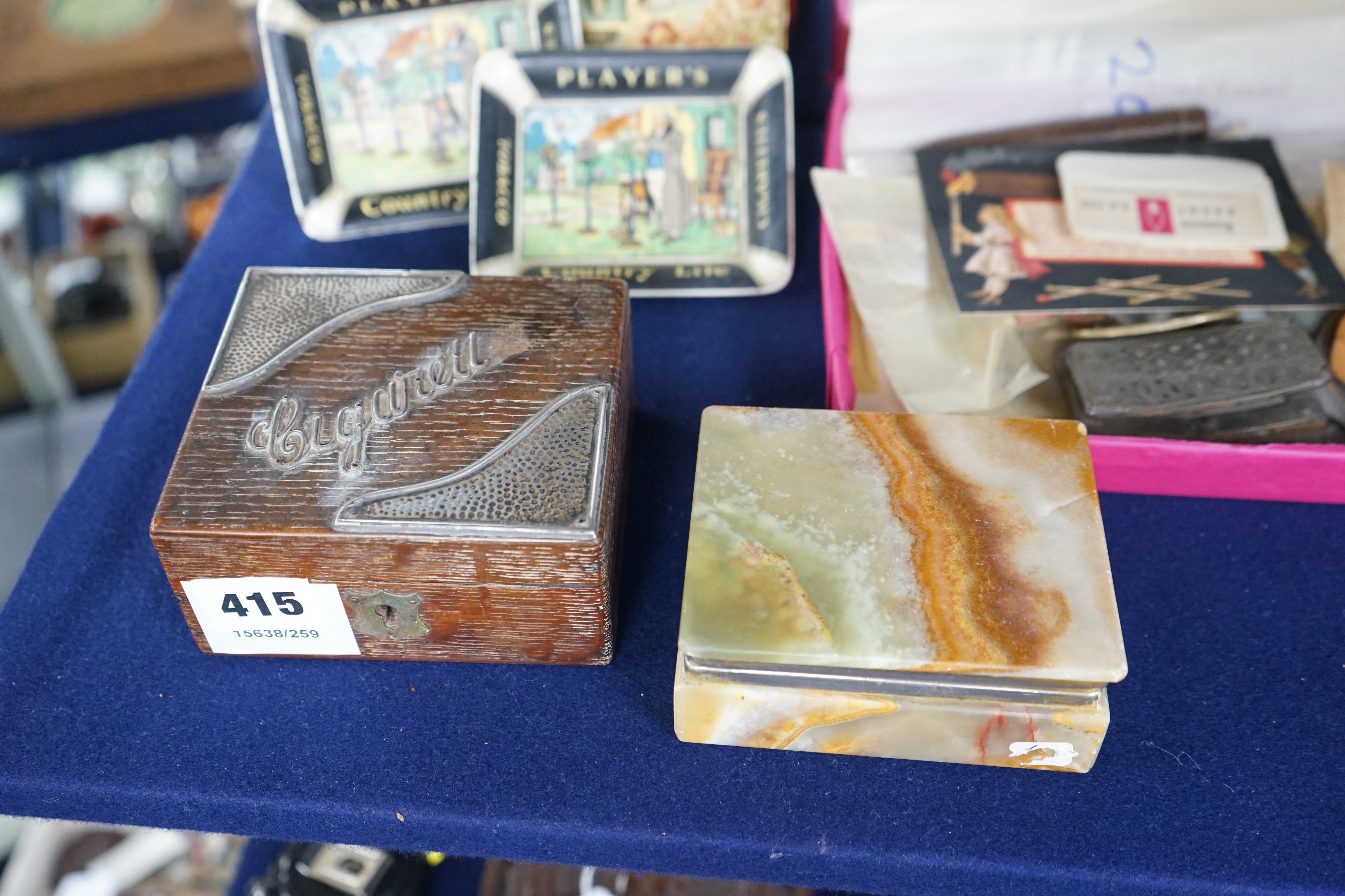 A collection of smoking accessories including an onyx cigarette box, an oak cigarette box, two Player’s ashtrays, a match box, cigarette box wrappers, etc. Condition - fair